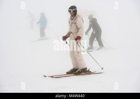 Group of skiers glide down the slopes of the Sierra de Béjar ski resort - La Covatilla, Salamanca, Spain a day of strong blizzard and fog. Stock Photo