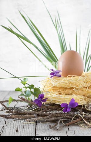 Nest of raw pasta with egg, green gras and violets, raw Italian  ingredients of spring season. Stock Photo