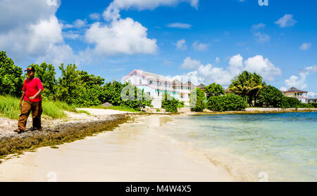 Young man, wearing Rastarian hat, walks on Anguillan beach. Anguilla. Stock Photo