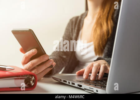 Woman holding smartphone and using laptop, business, freelance work at home concept Stock Photo
