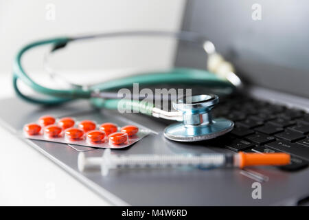 Pack of medicine pills, syringe and stethoscope laying on laptop keyboard. Medicine industry concept Stock Photo