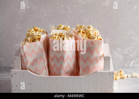 Golden caramel pop corn in paper bags in a white wooden box. Stock Photo