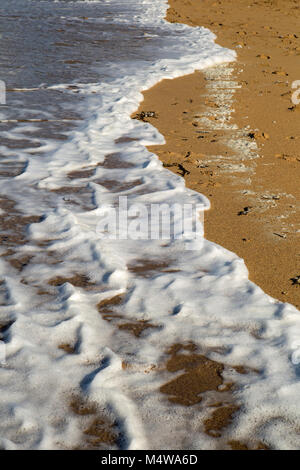White sea foam as the tide comes in on a sandy cornish beach Stock Photo