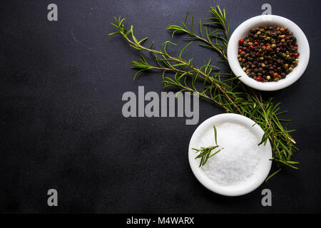 Rosemary, sea salt and pepper  in ceramic bowls on rustic wooden background with copyspace Stock Photo