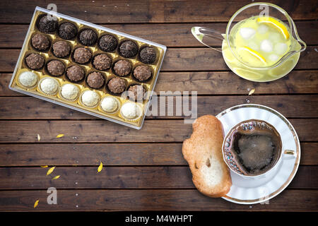 On the surface of the wooden table coffee Cup with croutons, chocolates, lemon with ice. Stock Photo