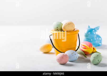 Easter composition with colored quail eggs candies in bucket and blue ceramic rabbit. Holidays concept with copy space. Stock Photo