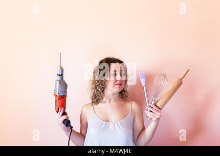 Beautiful curly woman holding man driller and kitchen tools. Gender equality, women's day concept. Stock Photo