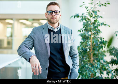 Waist up portrait of modern businessman posing in office building looking at camera and leaning on balcony railing Stock Photo