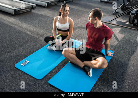 High angle  portrait of young sportive couple taking break while doing yoga on mats in modern gym, copy space Stock Photo