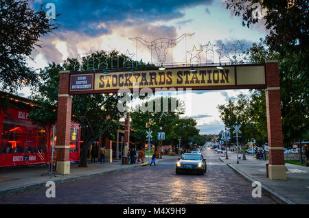 Fort Worth, Texas. Car passing under signpost at entrance to historic Fort Worth Stockyards lit up in early evening. Stock Photo