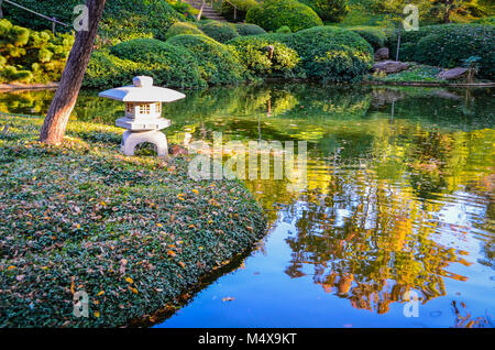 Japanese lantern and trimmed evergreen shrubs reflected in pond of Fort Worth Botanic Garden. Stock Photo