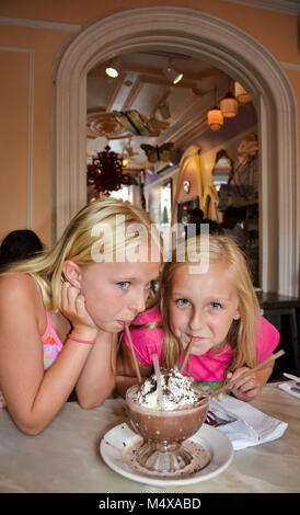 Vertical image of two blonde and blue eyed girls sip a Frozen Hot Chocolate dessert. Stock Photo