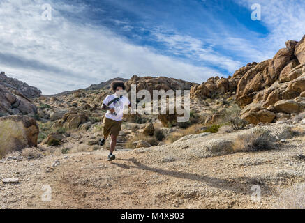 African-American man, wild afro hair flowing, runs downhill on Fortynine Palms Oasis trail in Joshua Tree National Park. Stock Photo