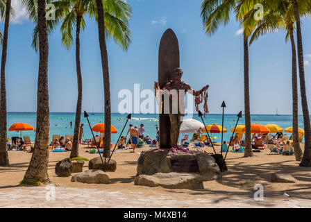 Duke Kahanamoku statue, Hawaiian surfer and Olympian, on Waikiki Beach with sunbathers, surfers, tourists, beach umbrellas in Honolulu, Hawaii, USA. Stock Photo