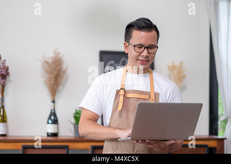 Asian male Barista cafe owner using laptop checking stock business inside coffee shop, food and drink business start up. Stock Photo