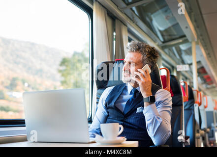 Handsome mature businessman travelling by train. A man with smartphone, making a phone call. Stock Photo