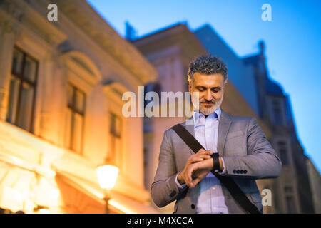 Handsome mature businessman with a smartwatch in a city in the evening, checking the time. Stock Photo