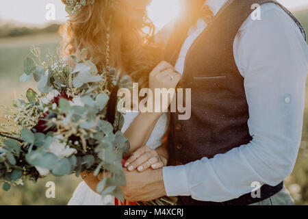 Unrecognizable young bride and groom outside in green nature at romantic sunset. Stock Photo