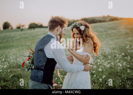 Beautiful young bride and groom outside in green nature at romantic sunset, having fun. Stock Photo