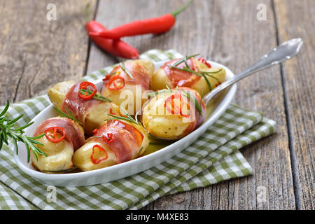 Hot rosemary potatoes stuffed with cheese and wrapped in South Tyrolean bacon, baked in olive oil with chili slices Stock Photo