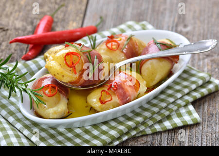 Hot rosemary potatoes stuffed with cheese and wrapped in South Tyrolean bacon, baked in olive oil with chili slices Stock Photo