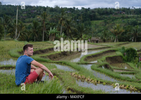 Young Man Traveler sitting and relaxing outdoor at rice fields on terraced in Bali Indonesia. Stock Photo