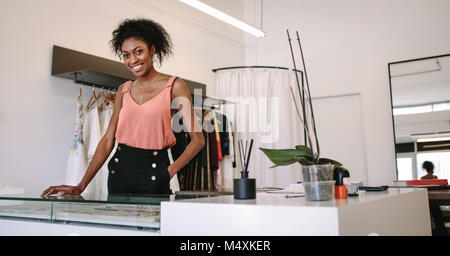 Female fashion designer standing at her desk in her boutique. Female dress designer in her cloth shop with designer clothes on display. Stock Photo