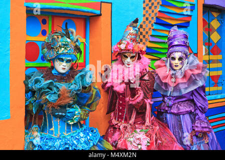Three costumed ladies in front of a colorful house during the Carnival of Venice (Carnevale di Venezia) in Burano, Italy Stock Photo