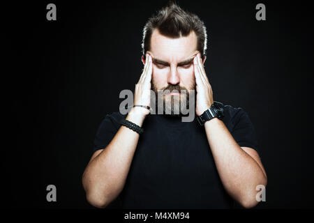 Terrible headache. Frustrated man touching head with hands and making face while standing against black background. Copy space for text Stock Photo
