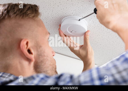 Close-up Of A Person's Hand Using Screwdriver To Install Smoke Detector On Ceiling At Home Stock Photo