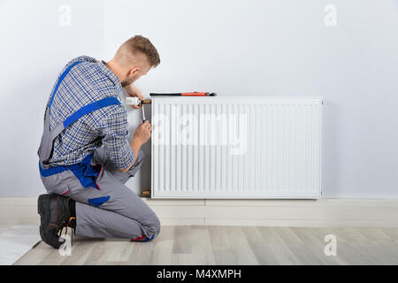 Rear View Of Male Plumber Fixing Thermostat With Screwdriver And Wrench On Radiator Stock Photo