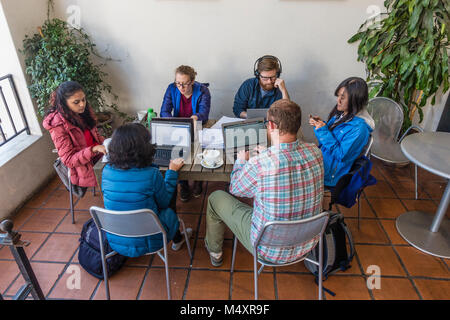 A group of six college students sit at a table at a coffee shop patio studying together with their laptops. Stock Photo