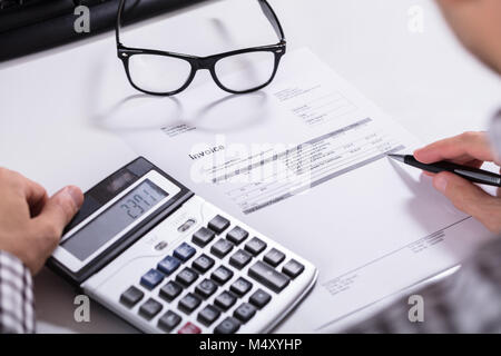 Close-up Of Businessman's Hands Calculating Invoice Using Calculator With Eyeglasses On Desk Stock Photo
