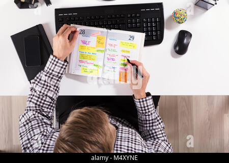 Elevated View Of Businessman's Hand Removing Stick Note From Diary With Computer Keyboard On Desk Stock Photo