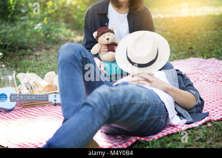 Casual handsome man put his head on knees his wife during picnic, outdoor, basket. Stock Photo