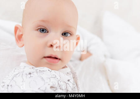 Adorable baby boy with blue eyes looking directly at camera trying to reach for it. Cute toddler close up portrait. Stock Photo