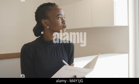 Charming serious african woman with natural make-up is thoughtfully looking aside while holding the documents in the office. Girl at the reception. Stock Photo