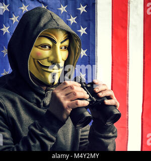 MILAN,ITALY, February, 2018: Hacker holding binoculars wear anonymus mask with american old glory flag in background.Editorial photo. Stock Photo