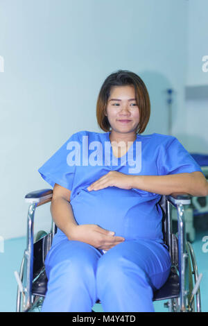 Asian pregnant woman is sitting on wheelchair at a hospital in Thailand. Stock Photo