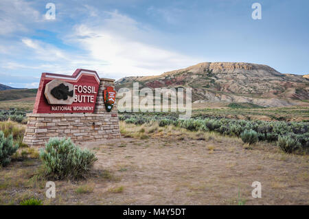 Fossil Butte National Monument sign in front of painted red hills in sagebrush desert. Kemmerer, Wyoming, USA Stock Photo