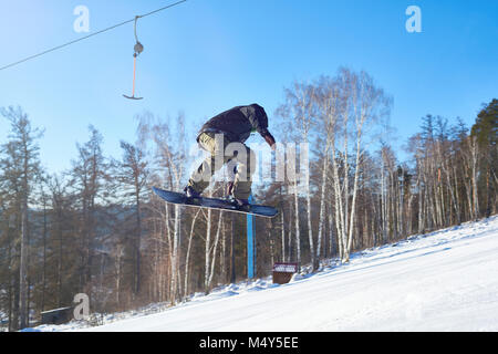 Portrait of young man performing snowboarding stunt flying high in air on mountain piste  at ski resort, copy space Stock Photo