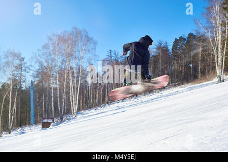 Portrait of young man performing snowboarding stunt jumping high in air and holding board backwards on mountain piste at ski resort, copy space Stock Photo