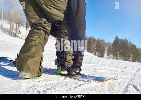 Back view close up of unrecognizable freestyle rider closing straps putting on snowboard ready to slide downhill om mountain piste, copy space Stock Photo