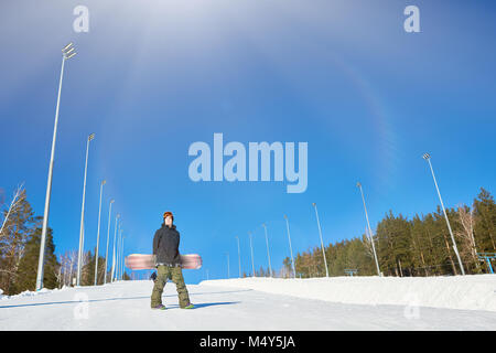 Full length wide angle portrait of modern young snowboarder posing on empty piste at ski resort against clear blue sky, copy space Stock Photo