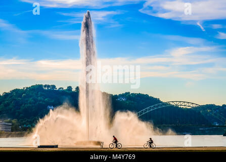 Two bicyclists pass water fountain at Point State Park along Ohio River in Pittsburgh, PA. Stock Photo