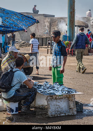Locals selling anchovy fish at a fish market in Essaouira, Morocco.  Blue colour throughout image. A customer has stopped to talk. Stock Photo