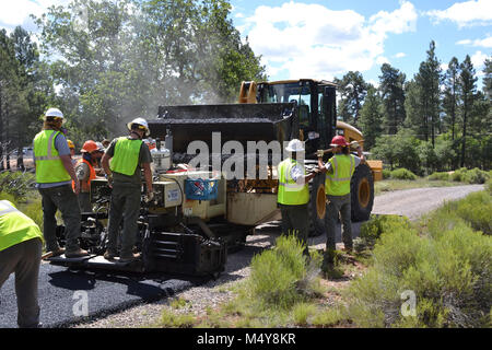 Workers help the front loader refill batch of asphalt onto the paving machine.  Between August 10 to September 10, 2016 the Greenway Trail between the IMAX Theater parking area in Tusayan and Center Road in Grand Canyon National Park will be closed while Grand Canyon's trail crew installs asphalt. The portion of the trail north of Center Road will not be affected.  While the trail closure is in effect, cyclists and hikers may ride the Tusayan shuttle (Purple Route) which is equipped with bicycle carrier racks. The shuttle connects Tusayan with the South Rim Visitor Center, a 20 minute ride eac Stock Photo