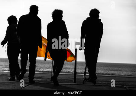 silhouette of four people standing near the beach with a colour flag between them. Stock Photo