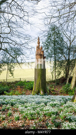 Carpet of snowdrops and carving of a castle on the stump of a dead tree trunk in woodland, Painswick Rococo Garden, Painswick, Gloucestershire Stock Photo