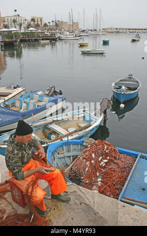 Local fisherman near the sea on Bari promenade with wooden boats, fish nets and old town in the background Stock Photo